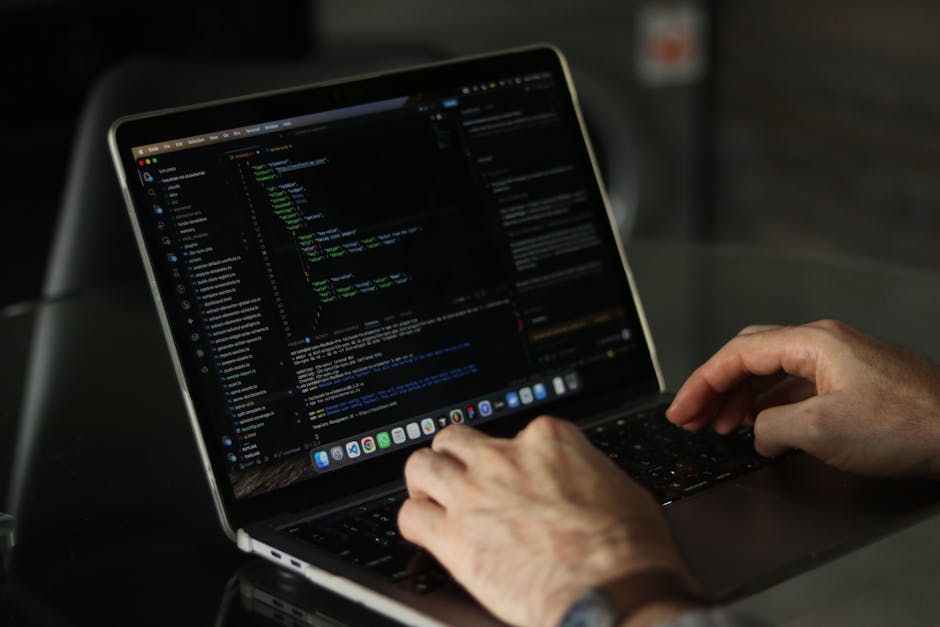A person working outdoors on a gardening project, viewed from above, using a laptop displaying lines of code on the screen. The person’s hands are visible, with one hand navigating the trackpad and th