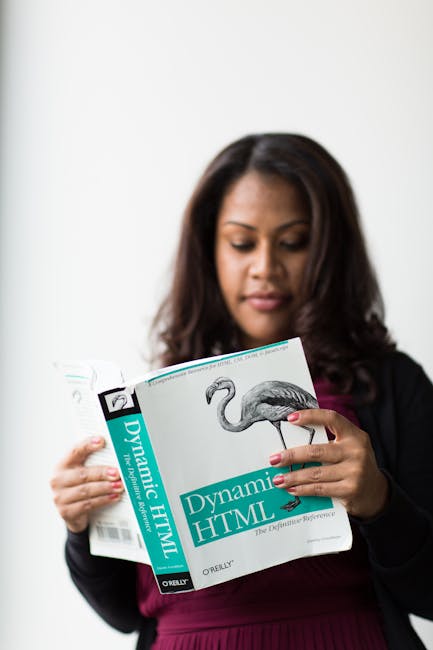 The image shows a woman with dark, wavy hair reading a book titled 'Dynamic HTML' by O'Reilly, which features a detailed illustration of a flamingo on the cover. She is indoors against a plain, light-